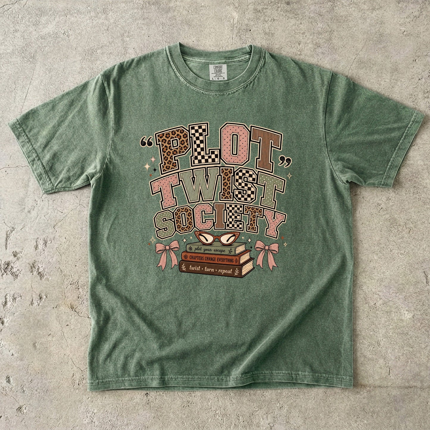 Moss Comfort Colors book lover T-shirt featuring the retro Plot Twist Society graphic with stacked books and glasses.