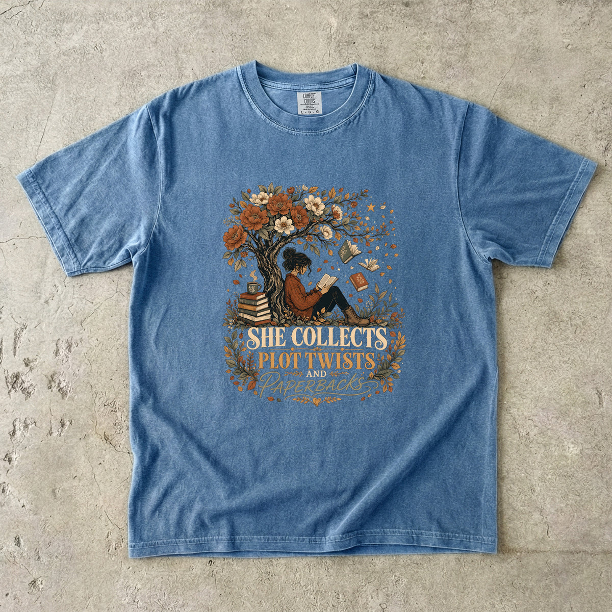 Blue Jean reading T-shirt featuring She Collects Plot Twists and Paperbacks with a reader beneath a flowering tree surrounded by books.