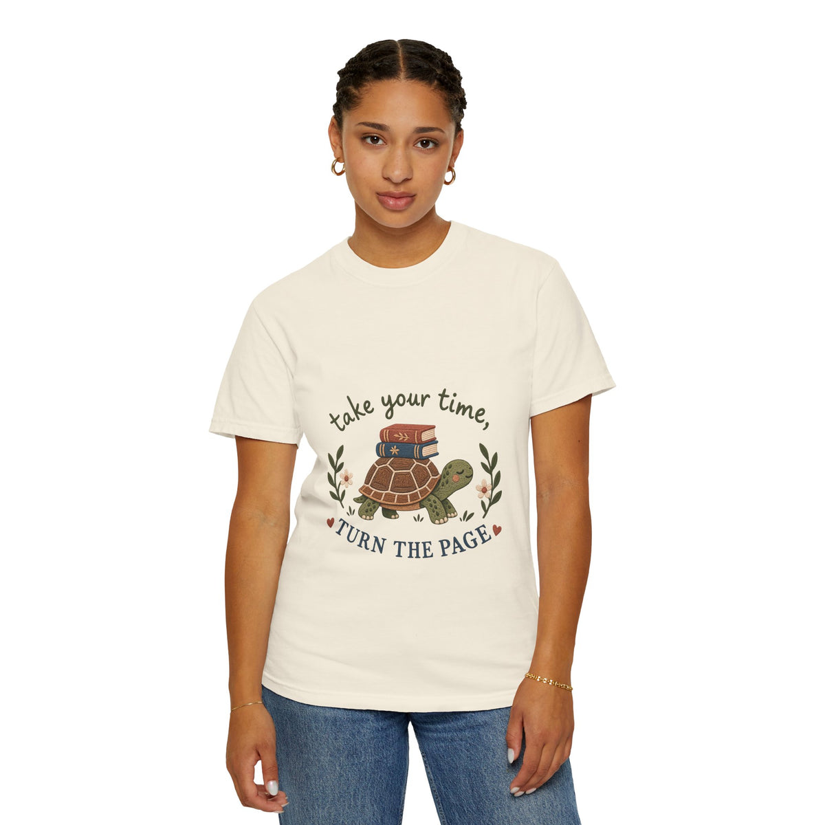 A woman modeling a ivory-colored graphic t-shirt with a turtle and book design, paired with blue jeans, against a plain white background.