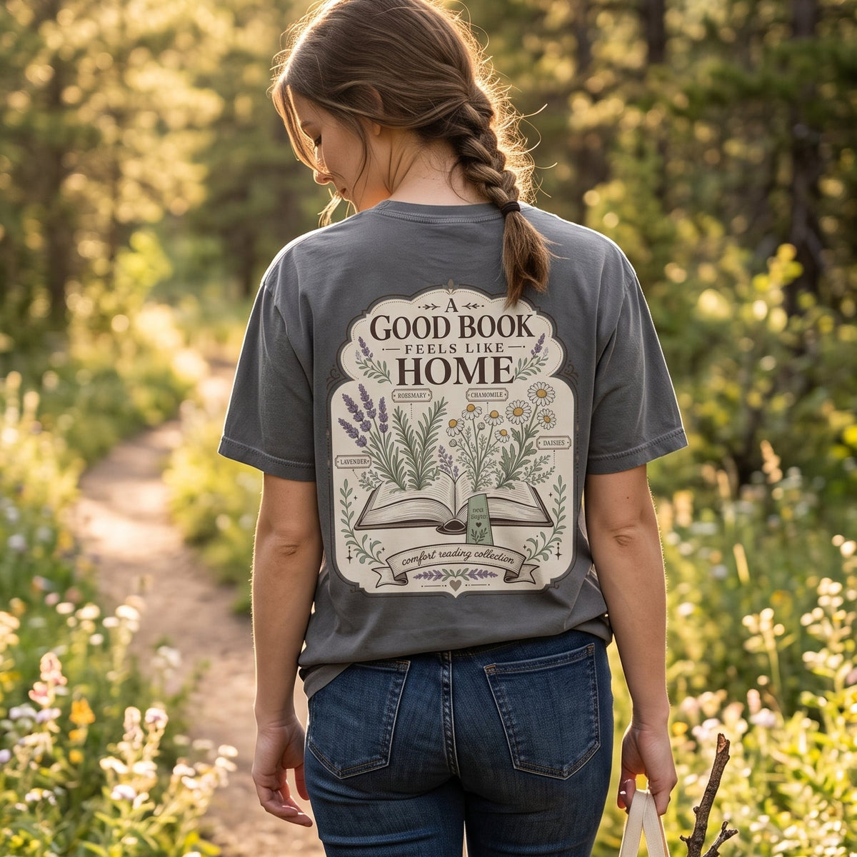 Woman wearing A Good Book Feels Like Home book lover T-shirt outdoors, featuring an open book with lavender, rosemary, chamomile and daisies.