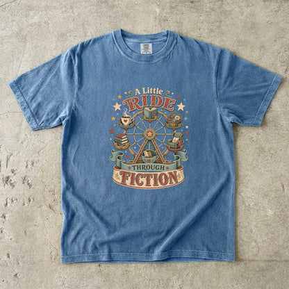 Front view of a Blue Jean Comfort Colors book lover T-shirt featuring the vintage "A Little Ride Through Fiction" illustration with books, tea, reading chair and Ferris wheel.