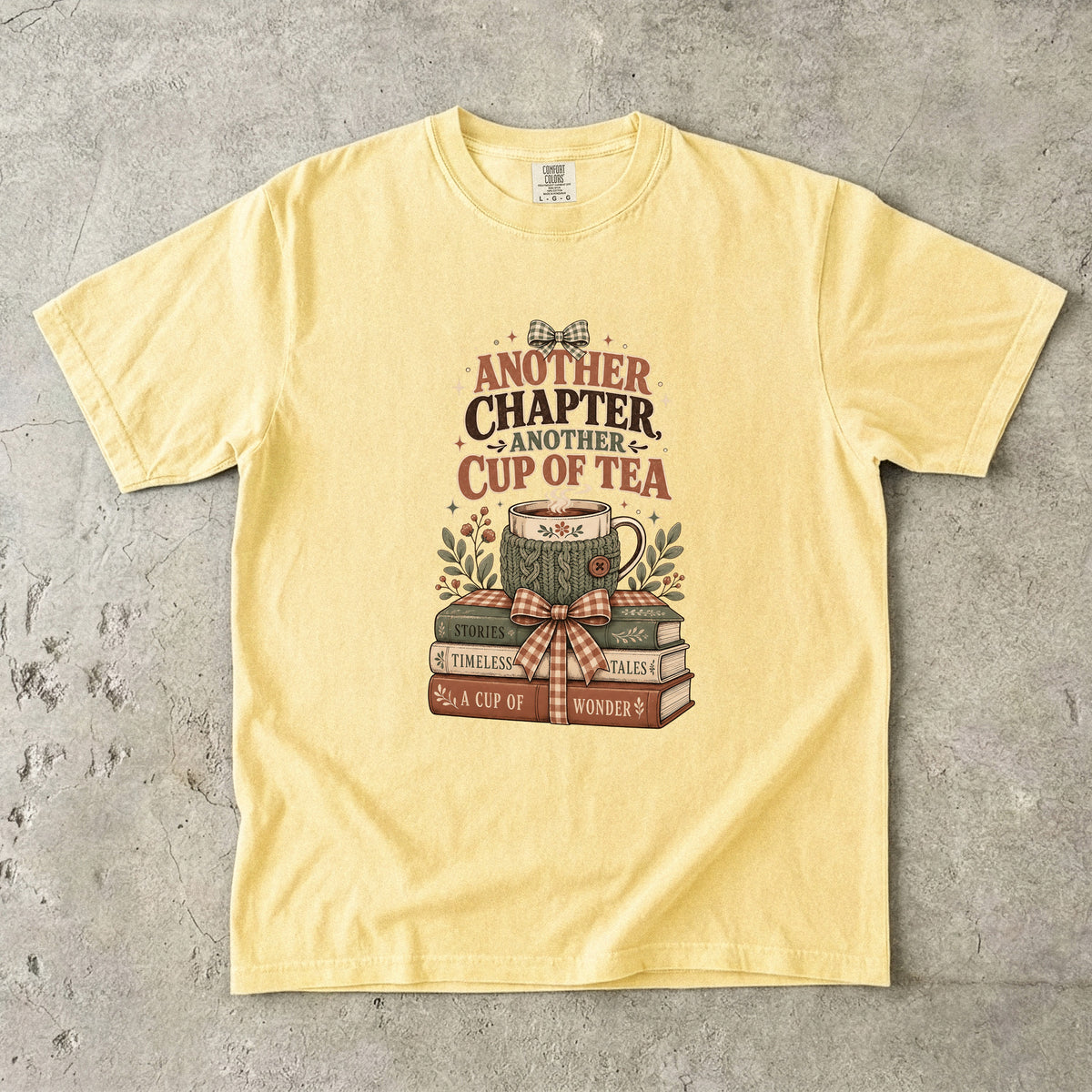 Another Chapter Another Cup of Tea reading shirt in Butter featuring a warm teacup and nostalgic book stack illustration.