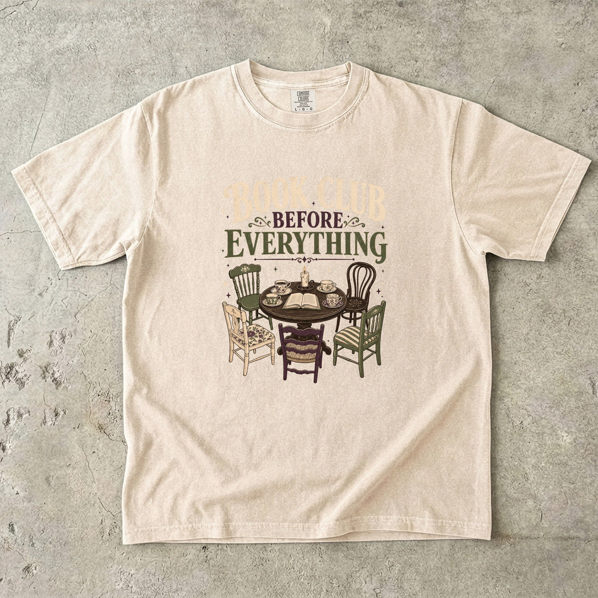 Ivory book club T-shirt featuring Book Club Before Everything with a vintage table, open book, teacups, candle and mismatched chairs.