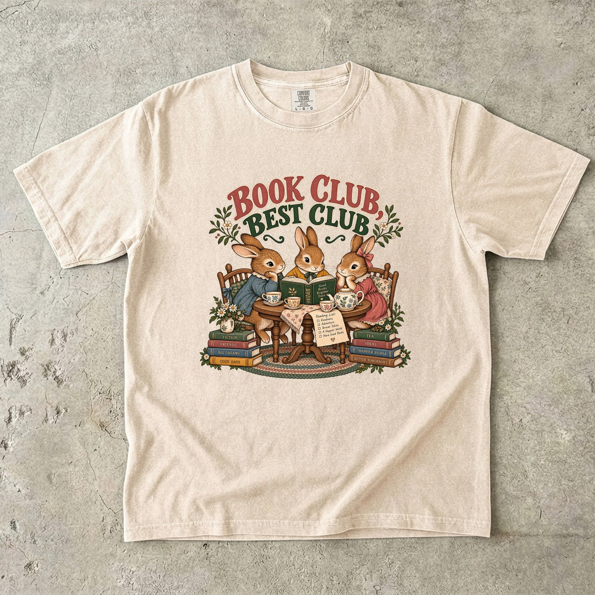 Ivory T-shirt featuring “Book Club, Best Club” with three rabbits reading together at a tea table, floral china, books and daisies.