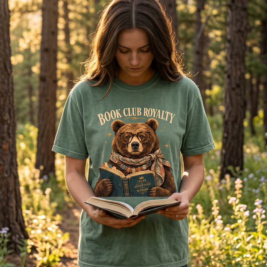 Reader wearing a Moss Book Club Royalty T-shirt while reading outdoors in a woodland setting.