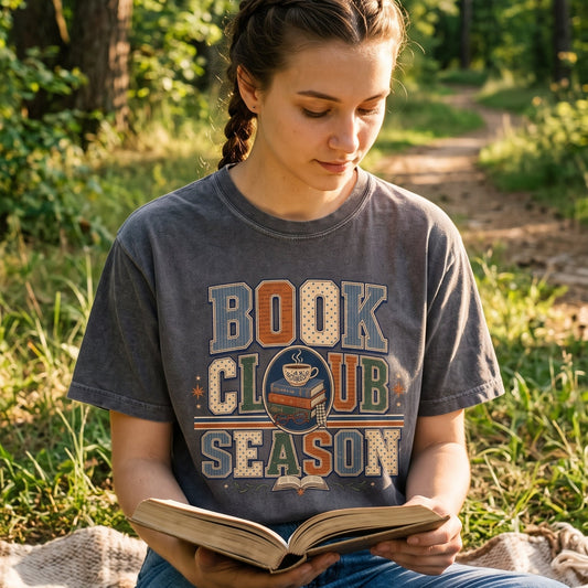 Reader wearing a Pepper Book Club Season T-shirt while sitting outdoors with an open book.