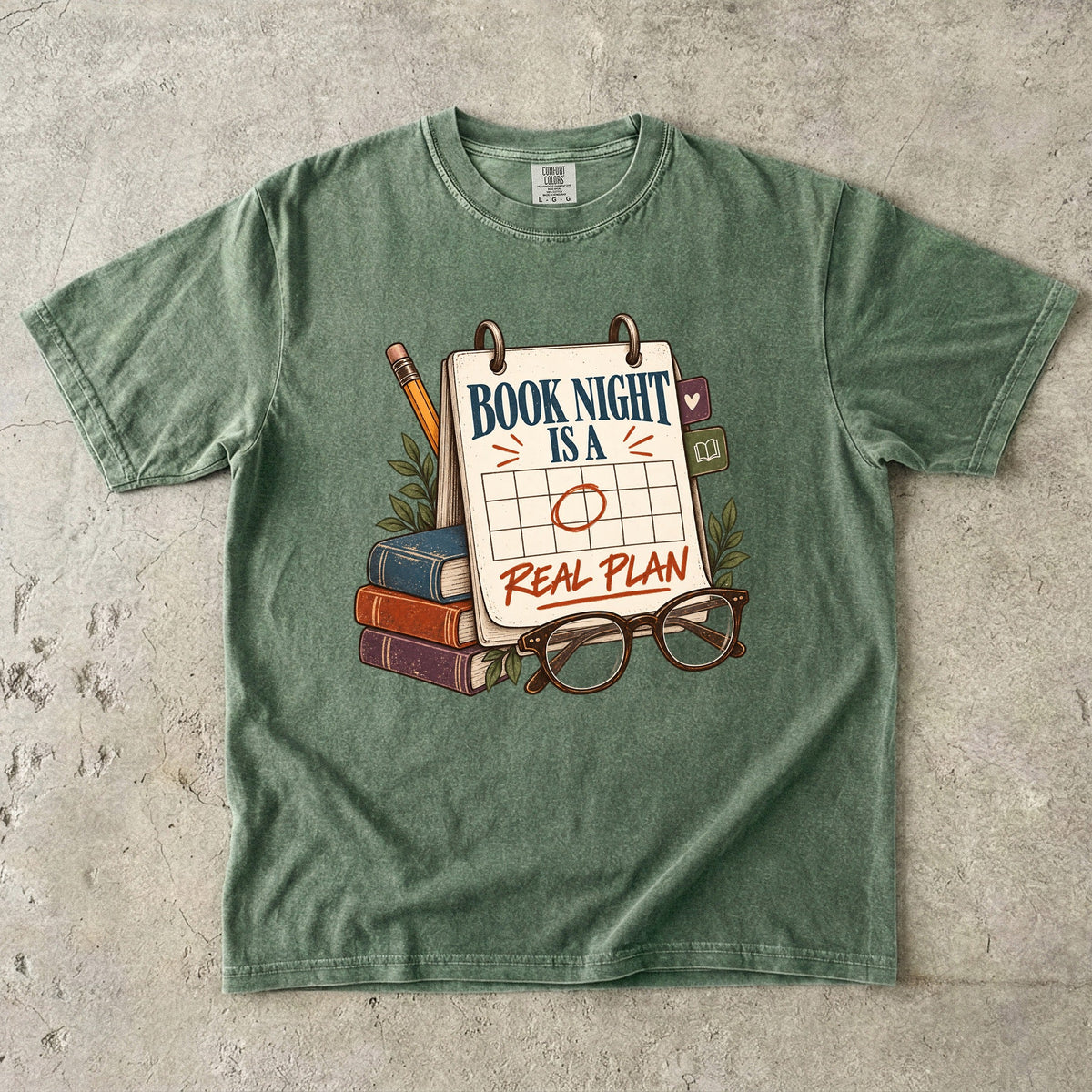Moss reading T-shirt with “Book Night Is a Real Plan” on a marked calendar beside books and glasses