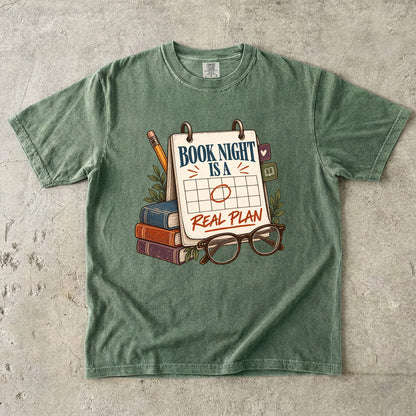 Moss reading T-shirt with “Book Night Is a Real Plan” on a marked calendar beside books and glasses