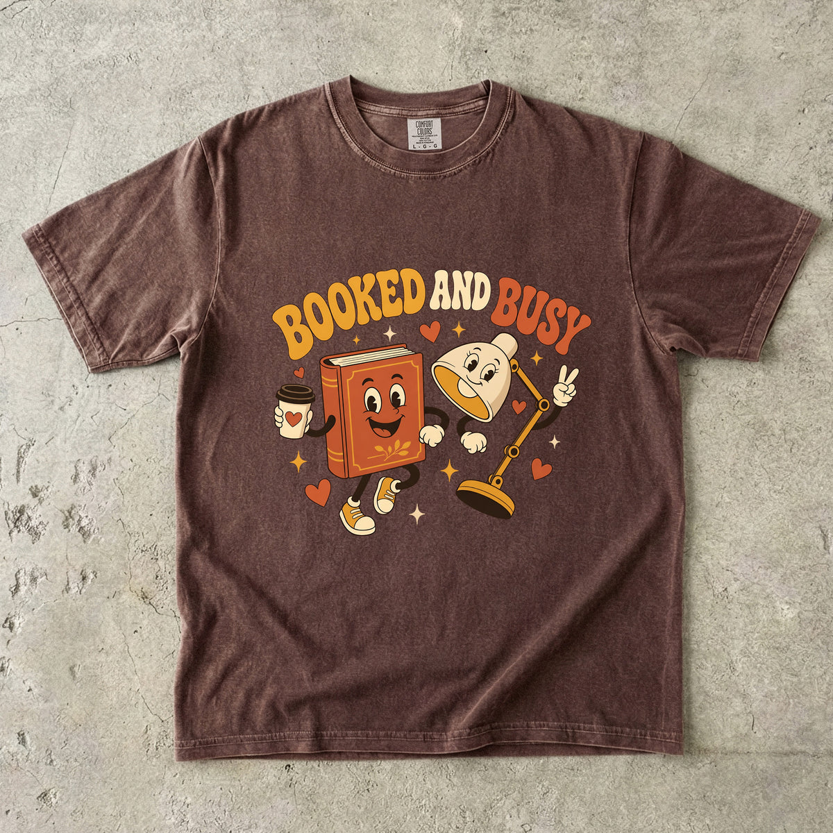 Espresso book lover T-shirt featuring Booked and Busy with a smiling book character, animated reading lamp, coffee cup, hearts and stars.