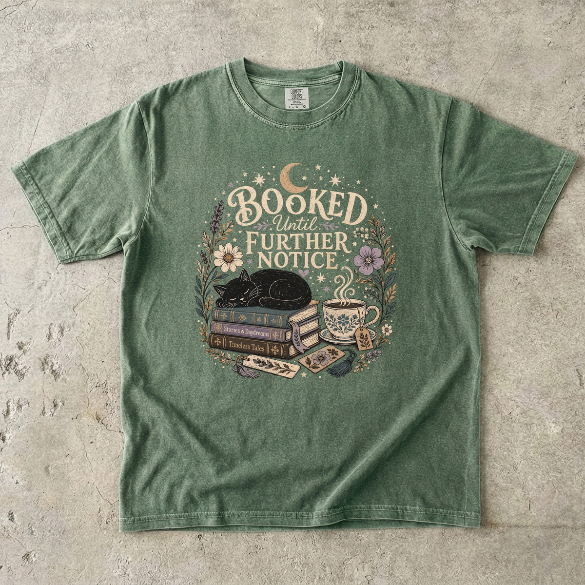 Booked Until Further Notice cat reading T-shirt with sleeping black cat, stacked books, teacup and flowers on Moss.