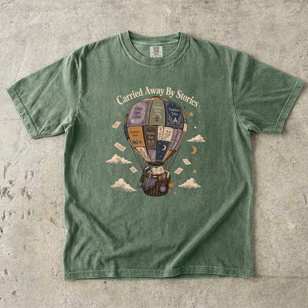 Carried Away by Stories book lover T-shirt in Moss featuring a hot air balloon made from books with floating pages and clouds