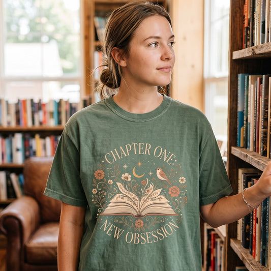 Chapter One: New Obsession book lover T-shirt with an illustrated open book, wildflowers, bird, crescent moon and stars.