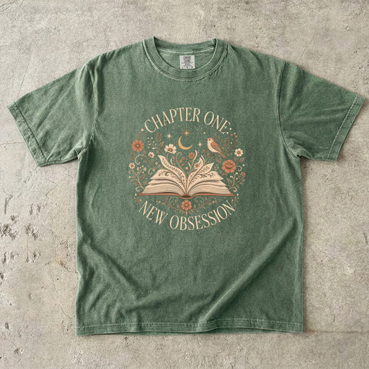 Moss book lover T-shirt featuring Chapter One: New Obsession with an open book, wildflowers, bird, crescent moon and stars.