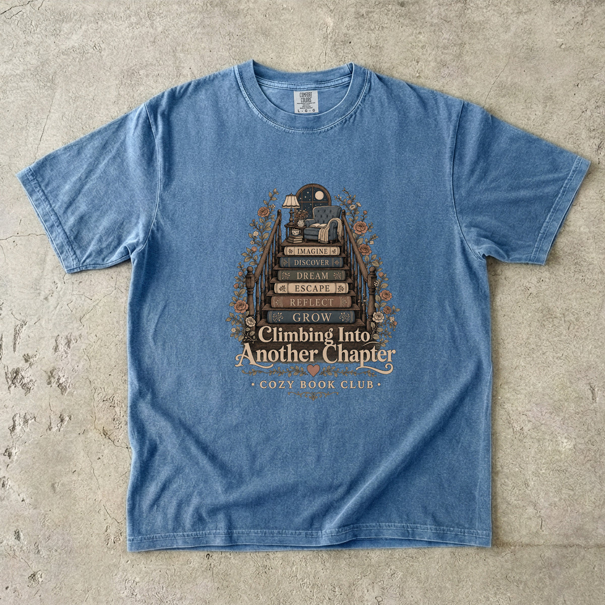 Climbing Into Another Chapter book lover T-shirt in Blue Jean featuring a staircase of books leading to a cozy reading chair