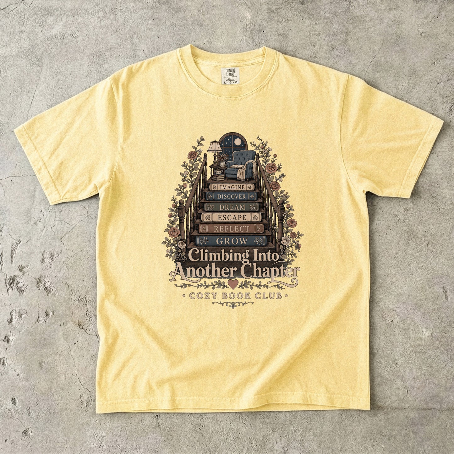 Front view of a Butter Comfort Colors® book lover T-shirt featuring the Climbing Into Another Chapter vintage reading illustration with stacked books, flowers and a cozy reading corner.