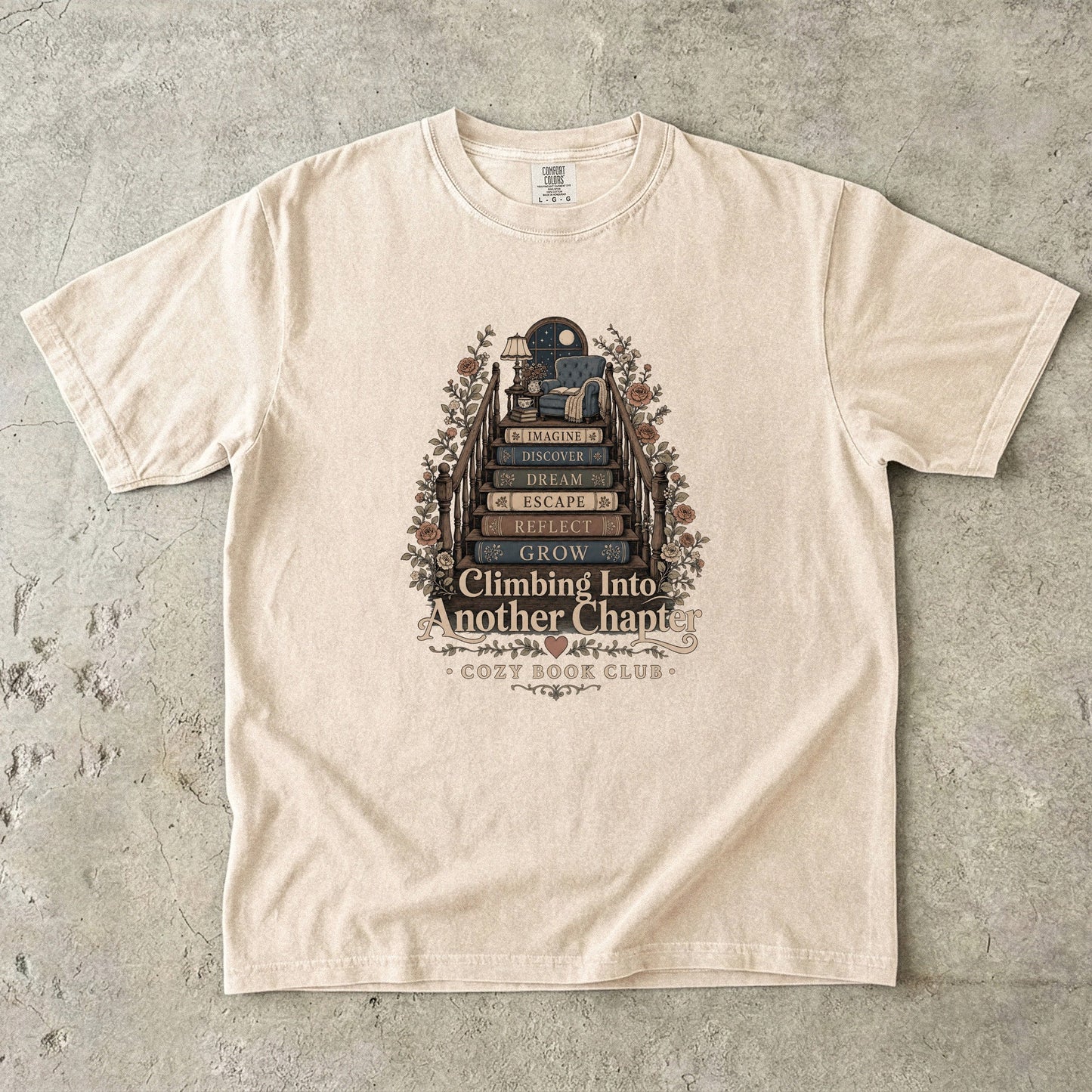 Front view of an Ivory Comfort Colors® book lover T-shirt featuring the Climbing Into Another Chapter design with stacked books, floral details and a moonlit reading retreat.