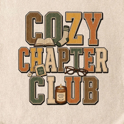 A ivory crewneck t-shirt laid flat on a textured gray concrete surface, featuring a retro-style graphic that reads 'COZY CHAPTER CLUB' in warm earthy tones with a small illustration of a mug and glasses.