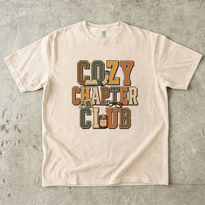 Ivory Comfort Colors Cozy Chapter Club reading T-shirt featuring retro lettering with books, tea, glasses and a candle.