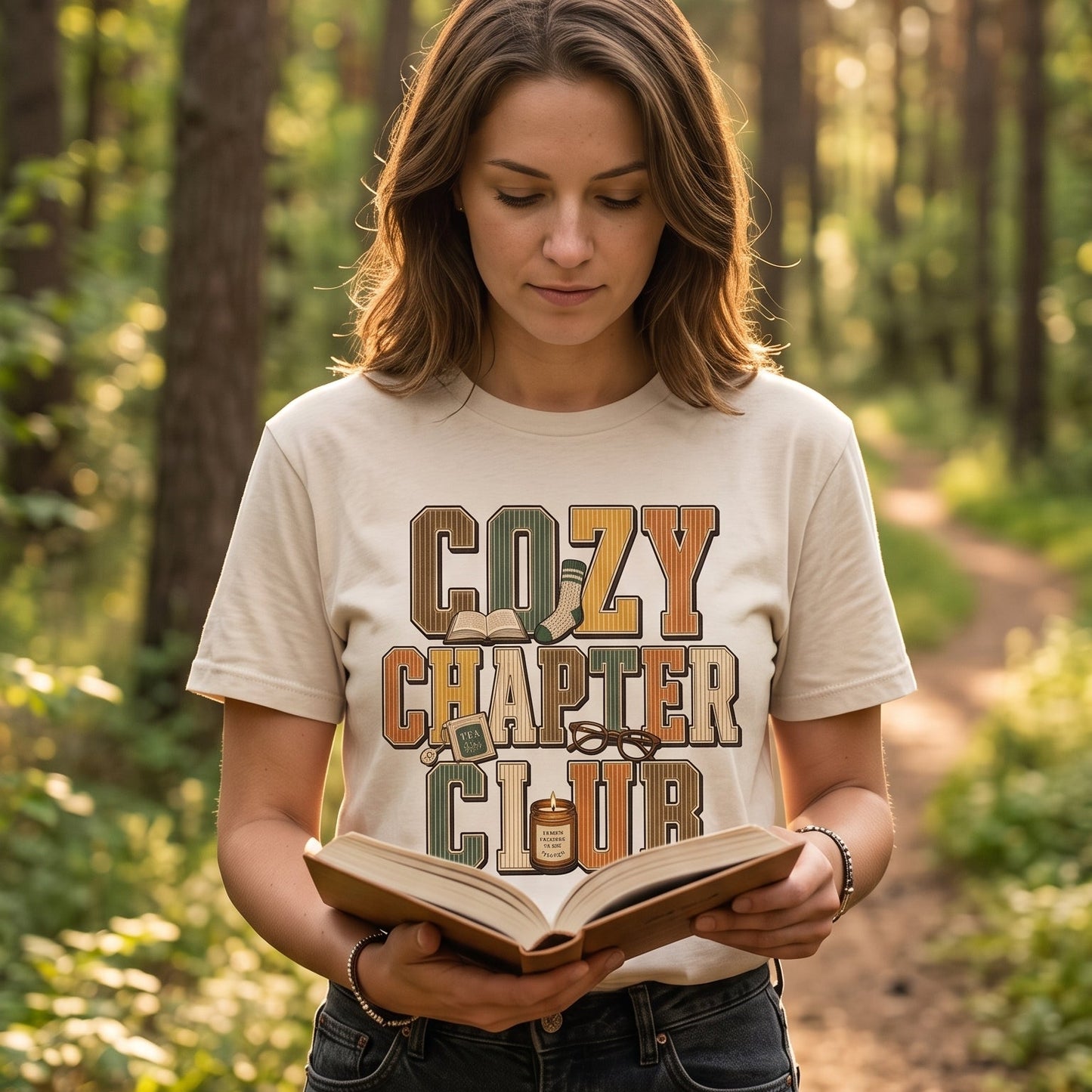 Woman reading outdoors while wearing an Ivory Cozy Chapter Club book lover T-shirt.