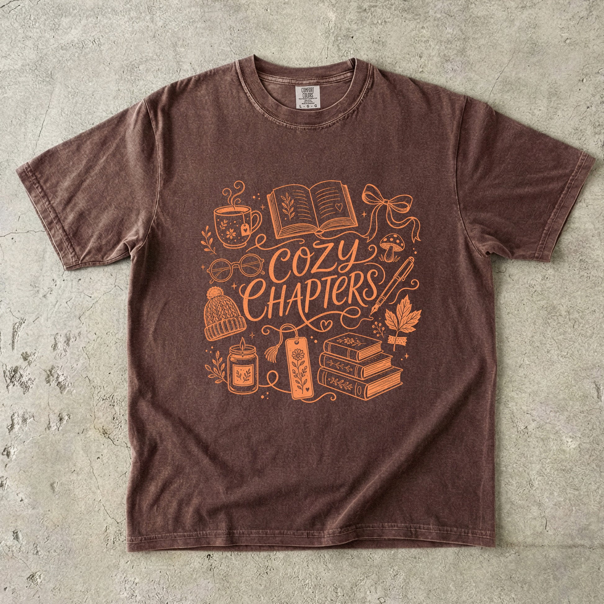 Espresso Comfort Colors reading shirt featuring orange Cozy Chapters artwork with books, tea, glasses and a candle.
