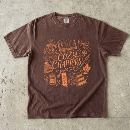 Espresso Comfort Colors reading shirt featuring orange Cozy Chapters artwork with books, tea, glasses and a candle.