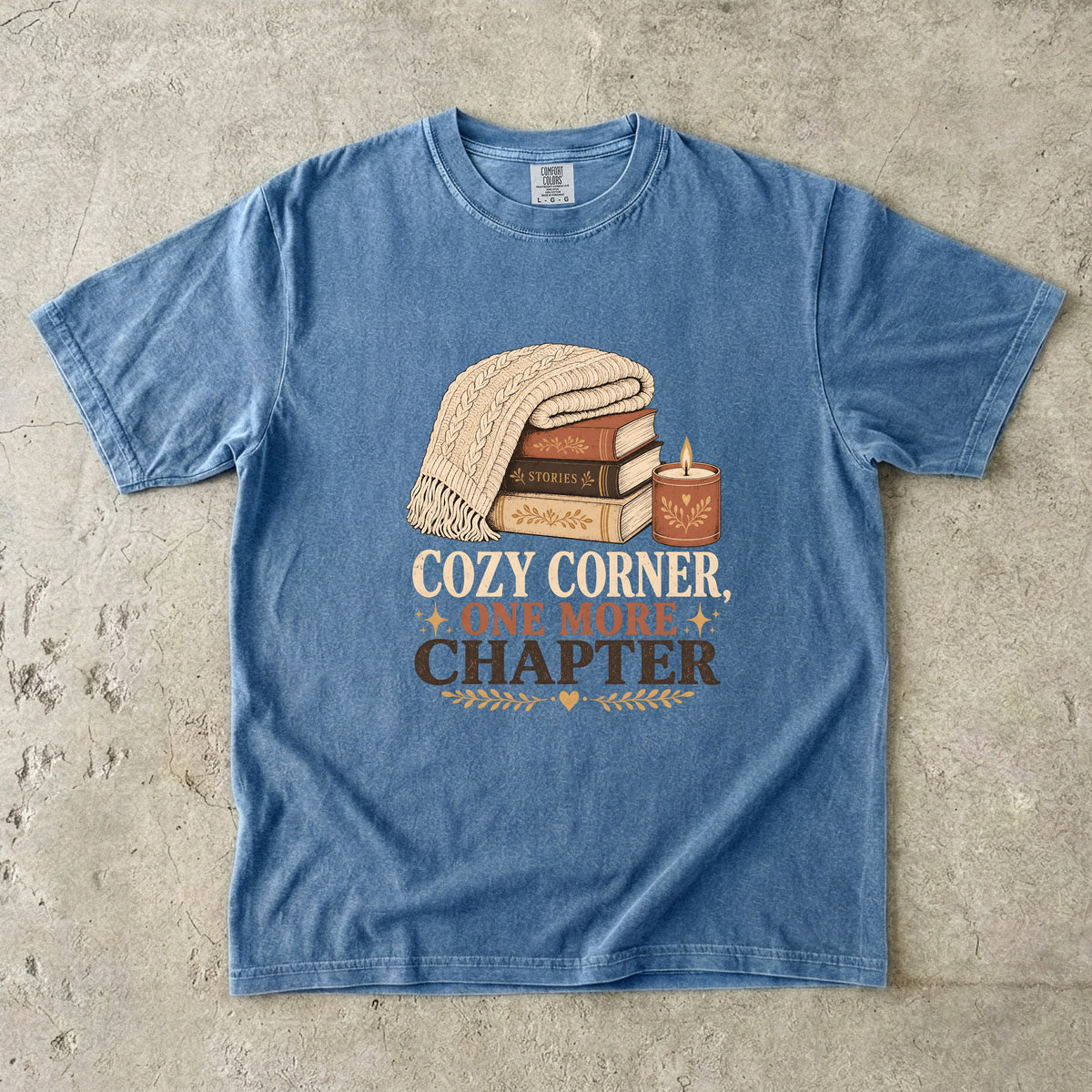 Blue Jean cozy reading T-shirt featuring Cozy Corner, One More Chapter with stacked books, a cable-knit blanket and glowing candle.