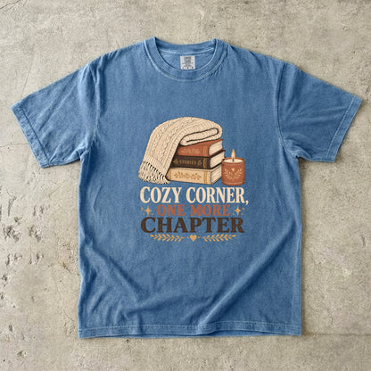Blue Jean cozy reading T-shirt featuring Cozy Corner, One More Chapter with stacked books, a cable-knit blanket and glowing candle.