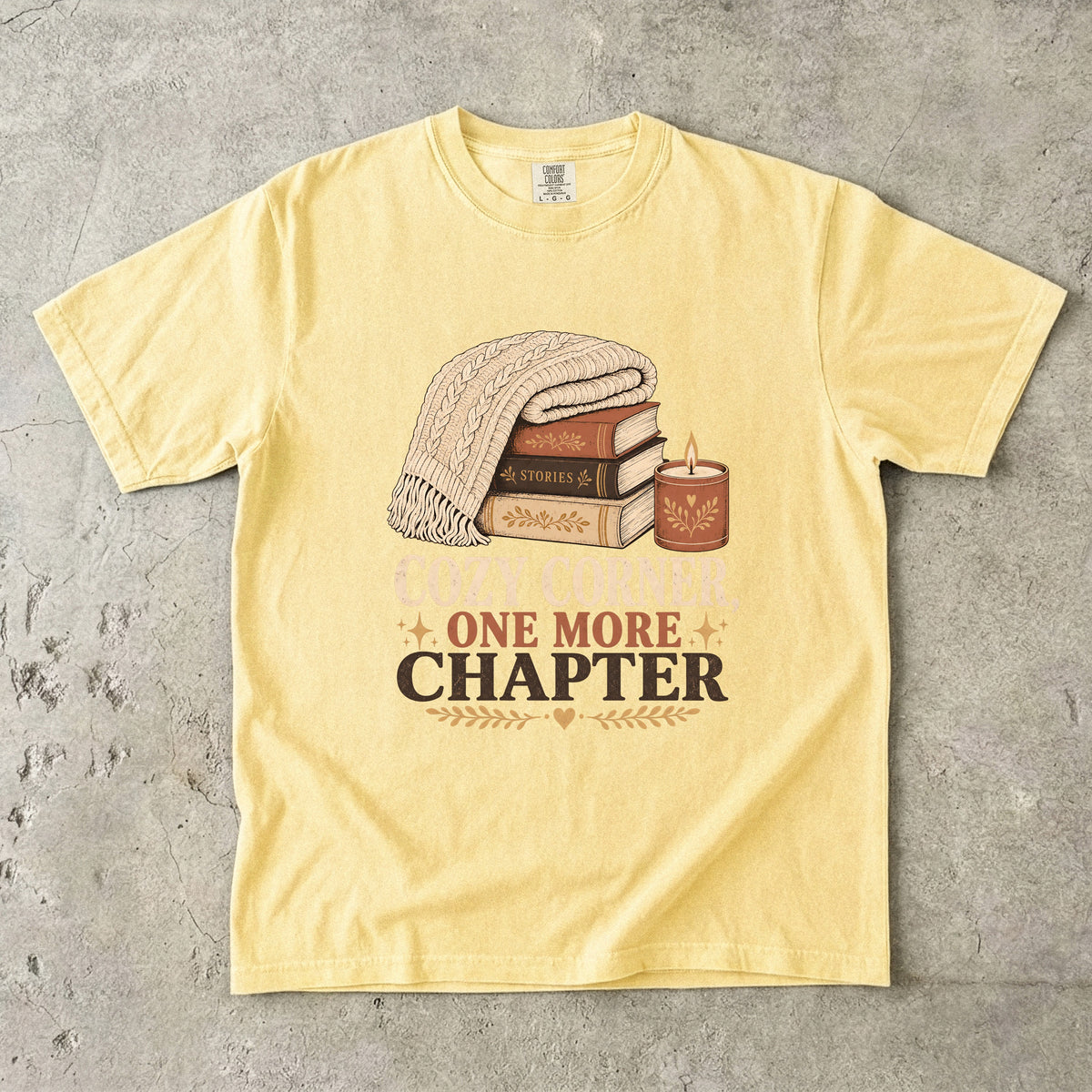 Butter cozy reading T-shirt featuring Cozy Corner, One More Chapter with stacked books, a cable-knit blanket and glowing candle.