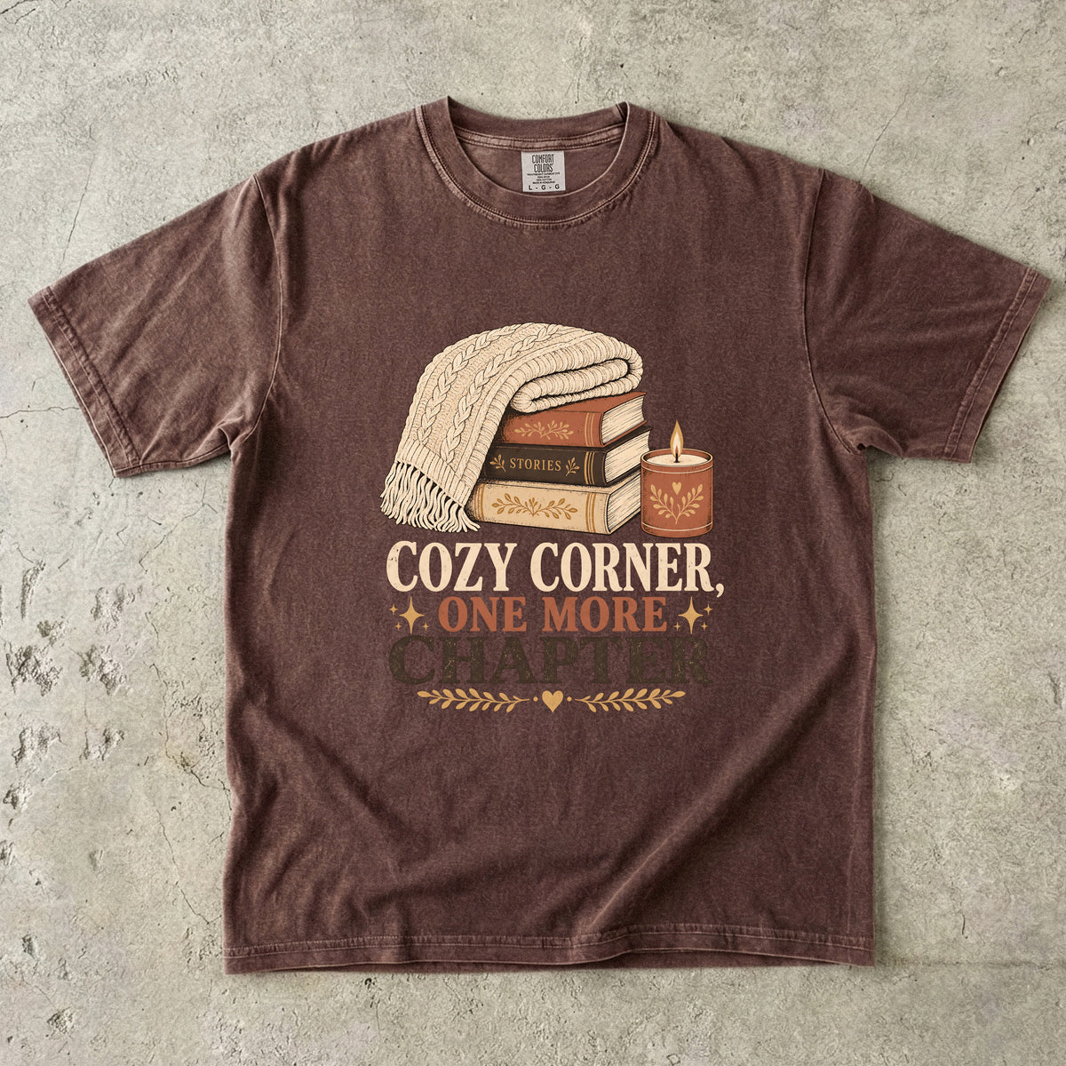 Espresso cozy reading T-shirt featuring Cozy Corner, One More Chapter with stacked books, a cable-knit blanket and glowing candle.