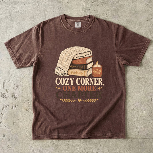 Espresso cozy reading T-shirt featuring Cozy Corner, One More Chapter with stacked books, a cable-knit blanket and glowing candle.