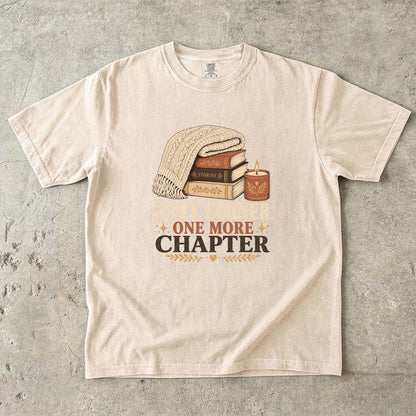 Ivory cozy reading T-shirt featuring Cozy Corner, One More Chapter with stacked books, a cable-knit blanket and glowing candle.