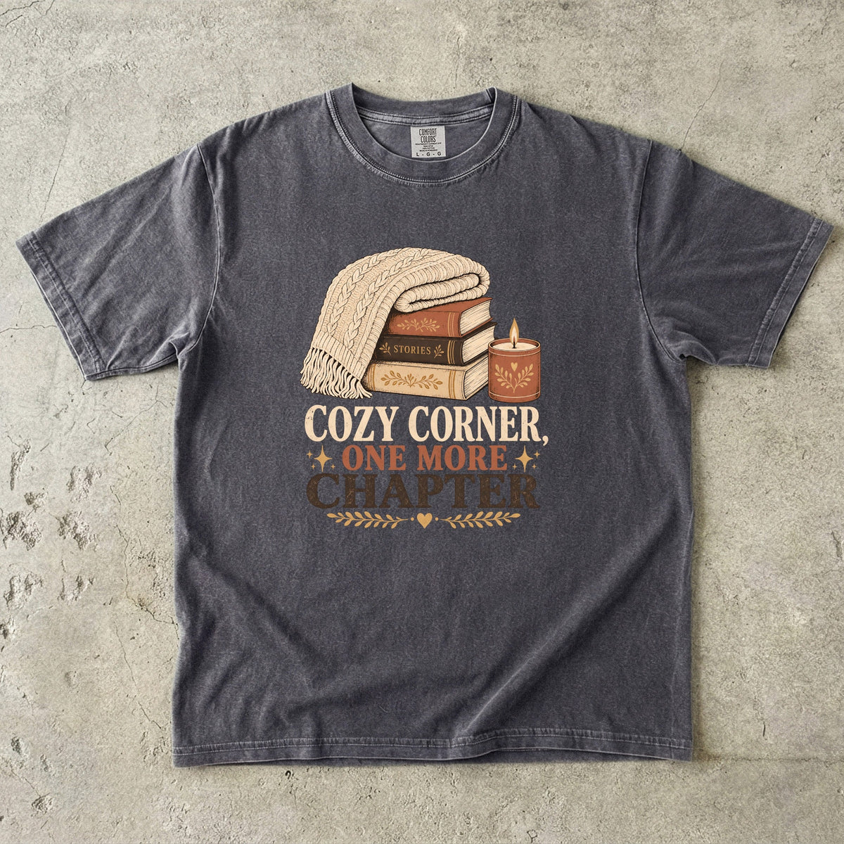 Pepper cozy reading T-shirt featuring Cozy Corner, One More Chapter with stacked books, a cable-knit blanket and glowing candle.