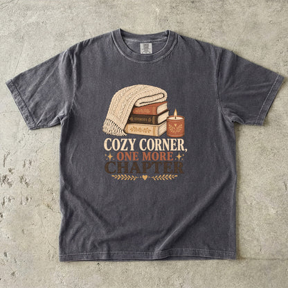 Pepper cozy reading T-shirt featuring Cozy Corner, One More Chapter with stacked books, a cable-knit blanket and glowing candle.