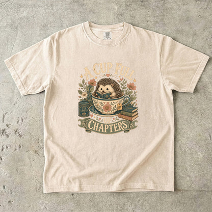 A Cup Full of Chapters hedgehog reading T-shirt in Ivory featuring a hedgehog reading inside a floral teacup with books