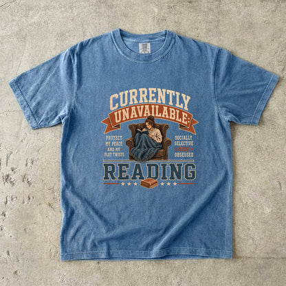 Blue Jean reading T-shirt featuring Currently Unavailable: Reading with a reader curled in a leather armchair beneath a blanket with a book.