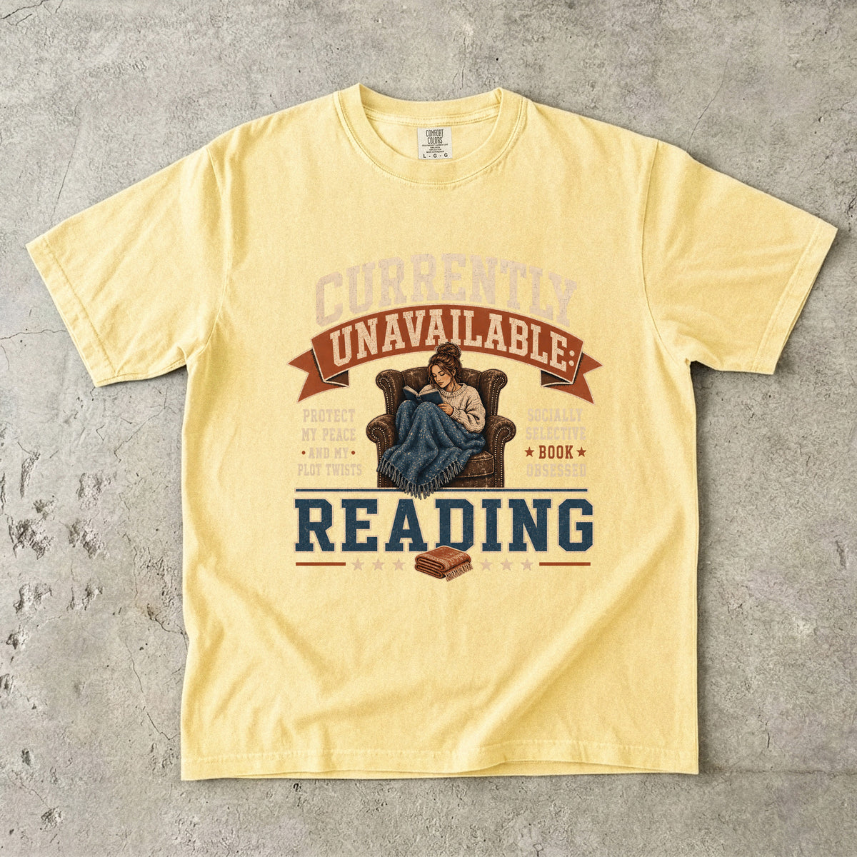 Butter reading T-shirt featuring Currently Unavailable: Reading with a reader curled in a leather armchair beneath a blanket with a book.
