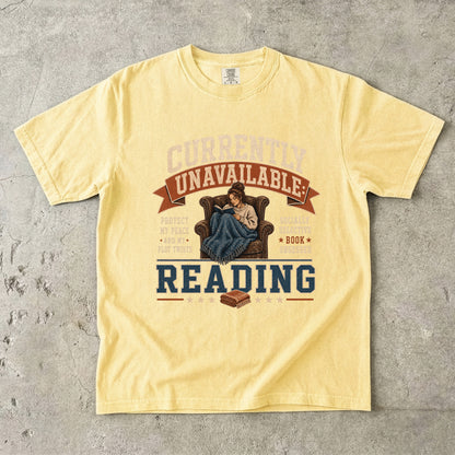 Butter reading T-shirt featuring Currently Unavailable: Reading with a reader curled in a leather armchair beneath a blanket with a book.