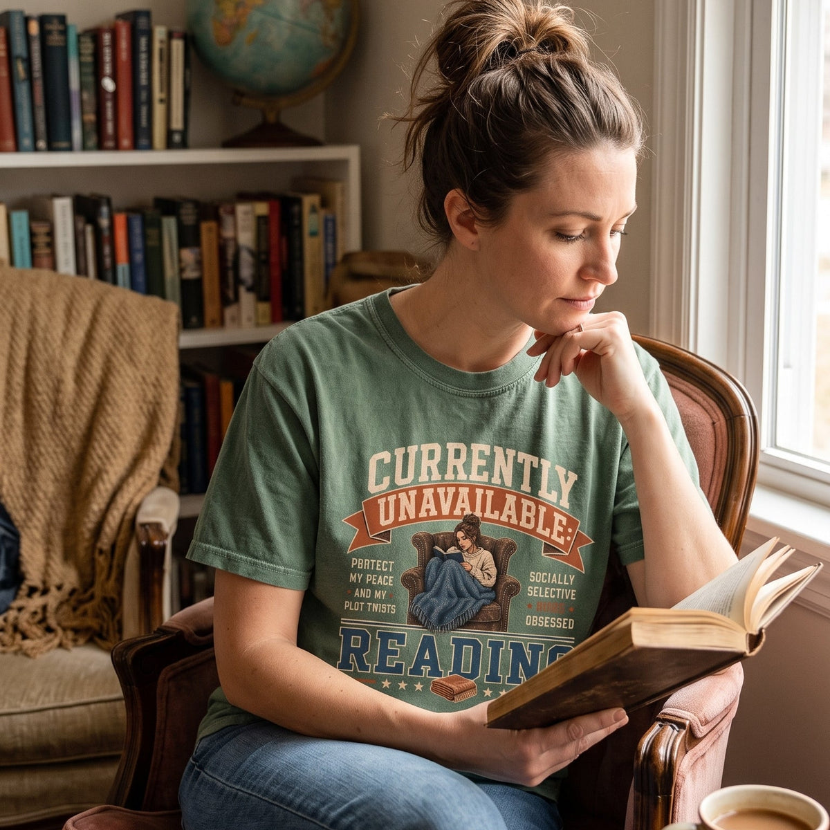 Currently Unavailable: Reading T-shirt featuring a book-obsessed reader curled in a leather armchair beneath a blanket.