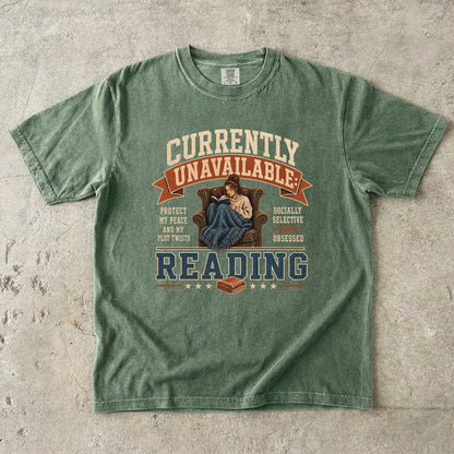 Moss reading T-shirt featuring Currently Unavailable: Reading with a reader curled in a leather armchair beneath a blanket with a book.