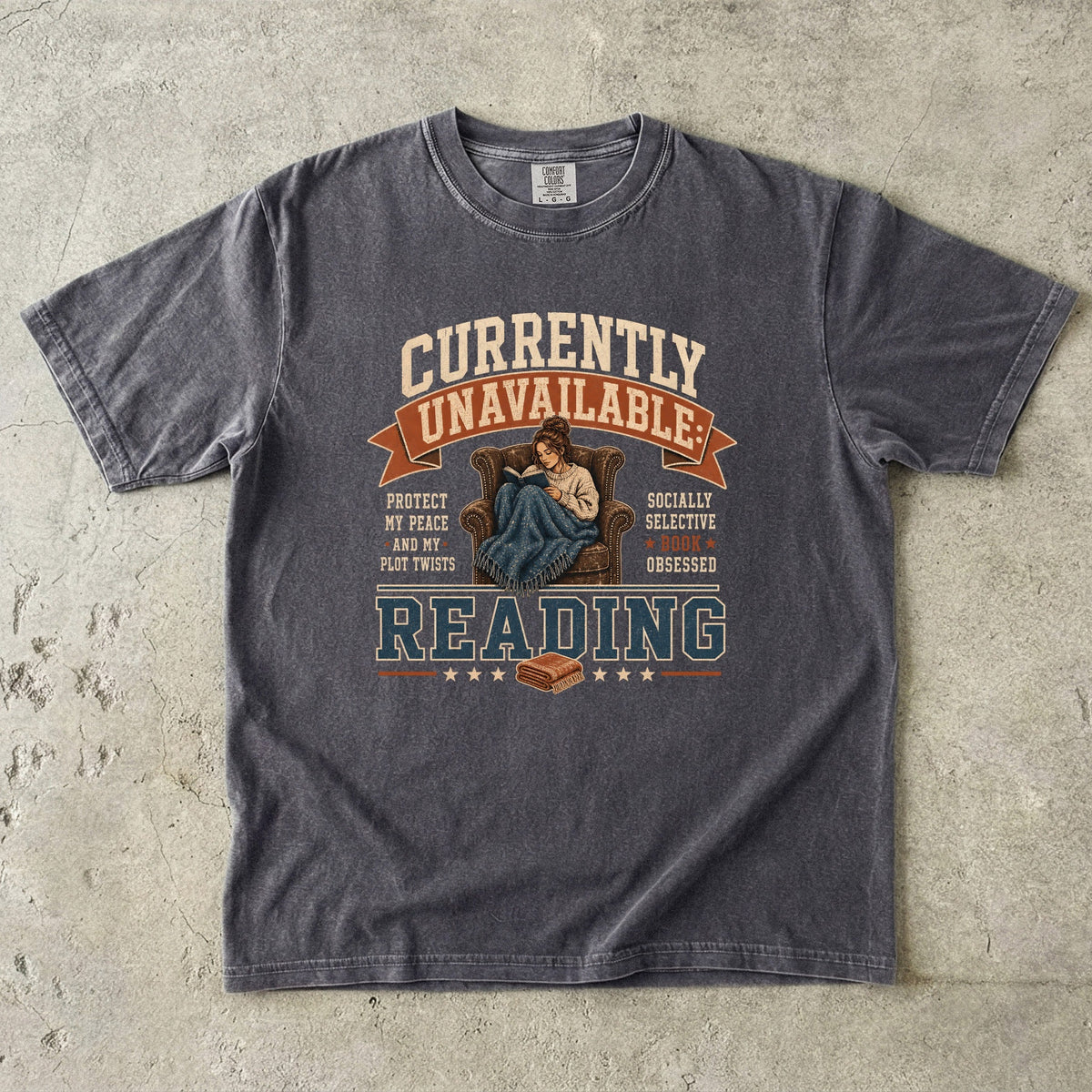 Pepper reading T-shirt featuring Currently Unavailable: Reading with a reader curled in a leather armchair beneath a blanket with a book.