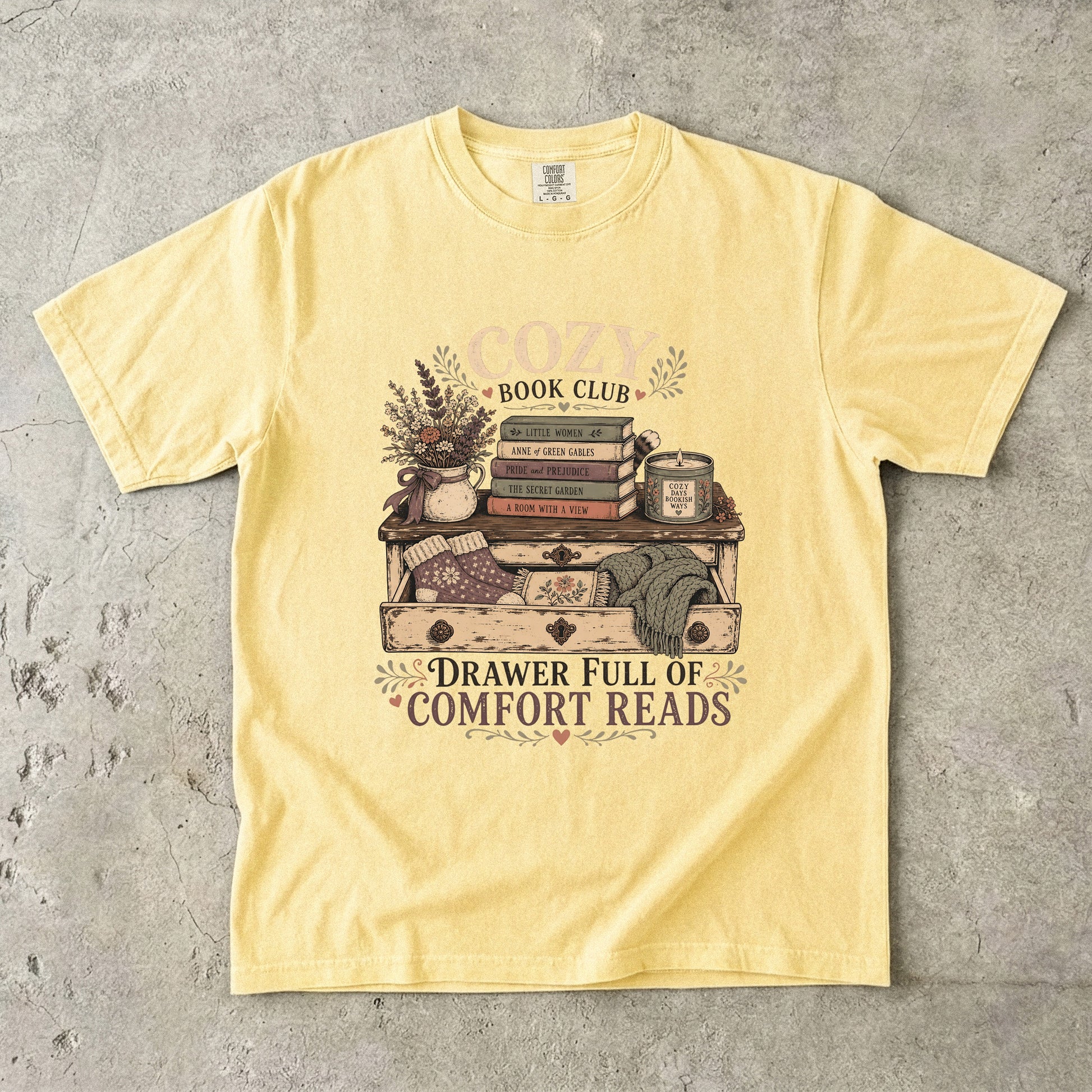 Drawer Full of Comfort Reads reading T-shirt in Butter featuring stacked books, candle, flowers, knitted socks and blankets