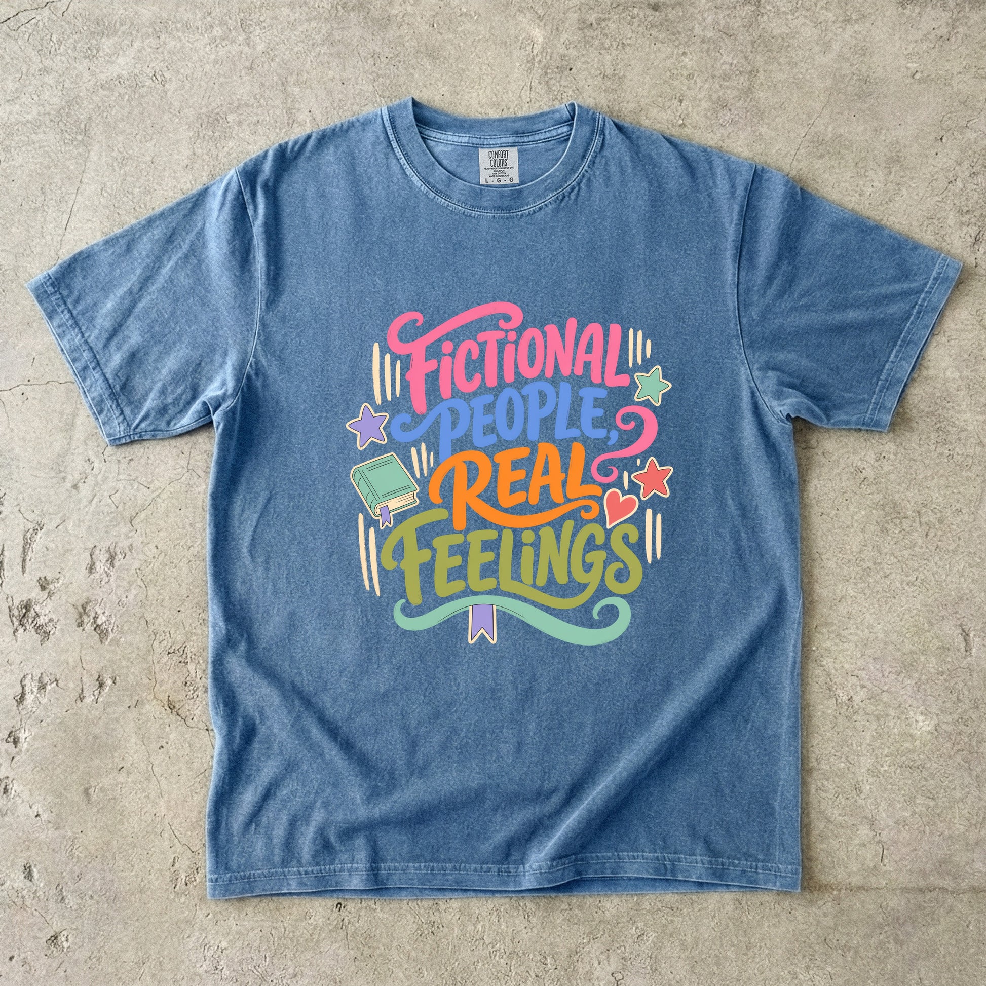 Blue Jean Comfort Colors bookish T-shirt featuring colourful Fictional People, Real Feelings typography with book and heart details.