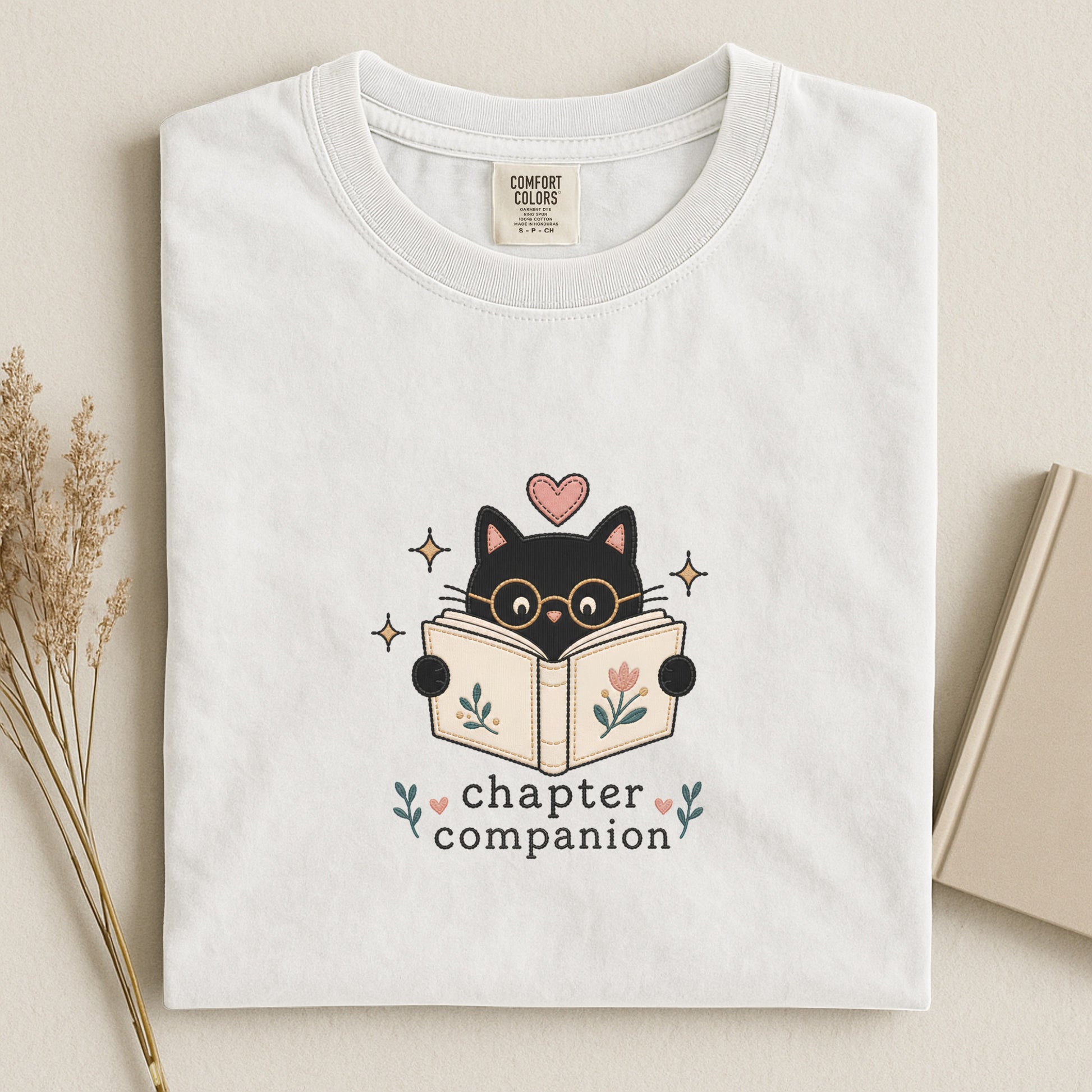 Close-up of the Chapter Companion cat and book illustration printed on a white Comfort Colors® T-shirt by Flourish Creation Labs.