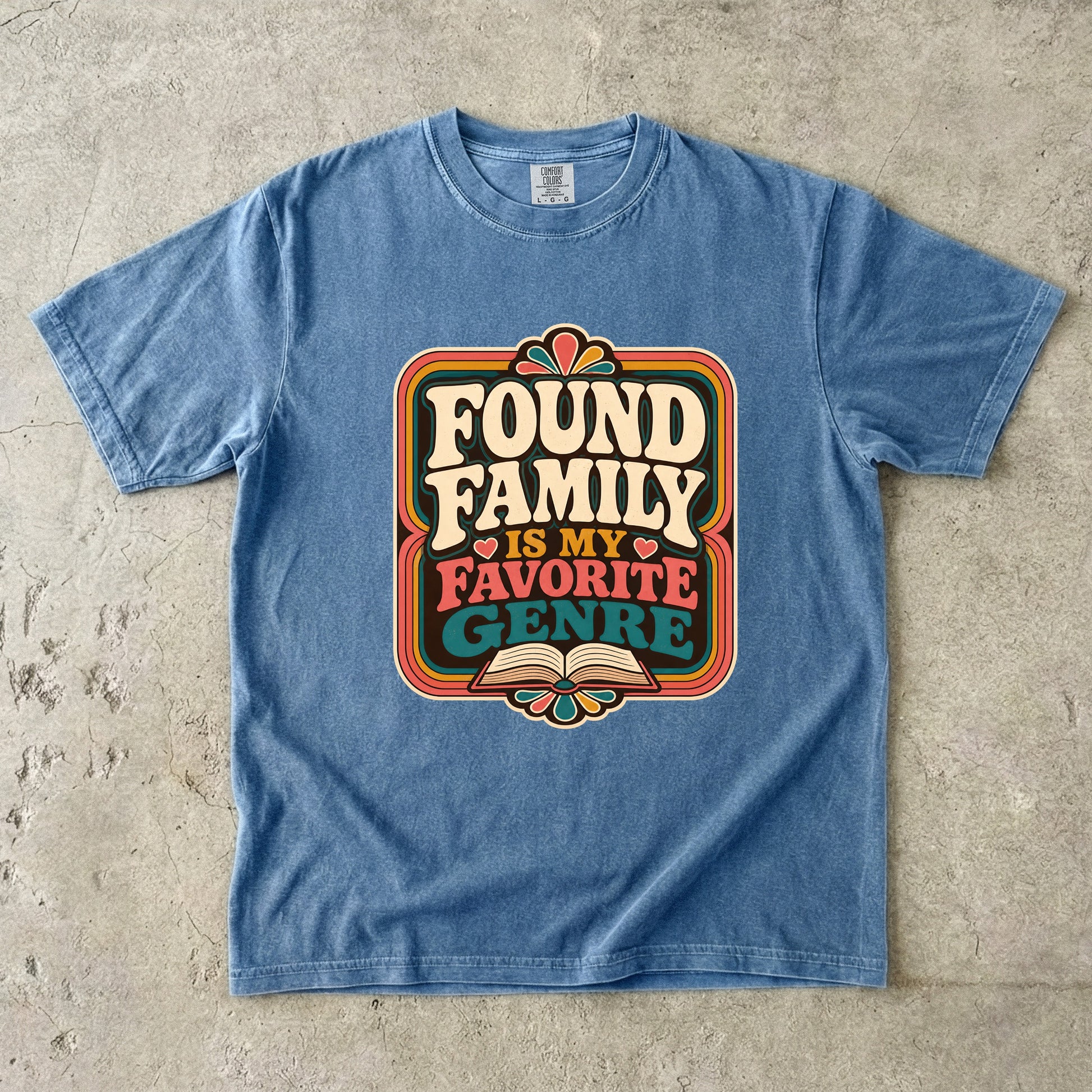 Blue Jean Comfort Colors book lover shirt featuring colourful Found Family Is My Favorite Genre typography and book artwork.