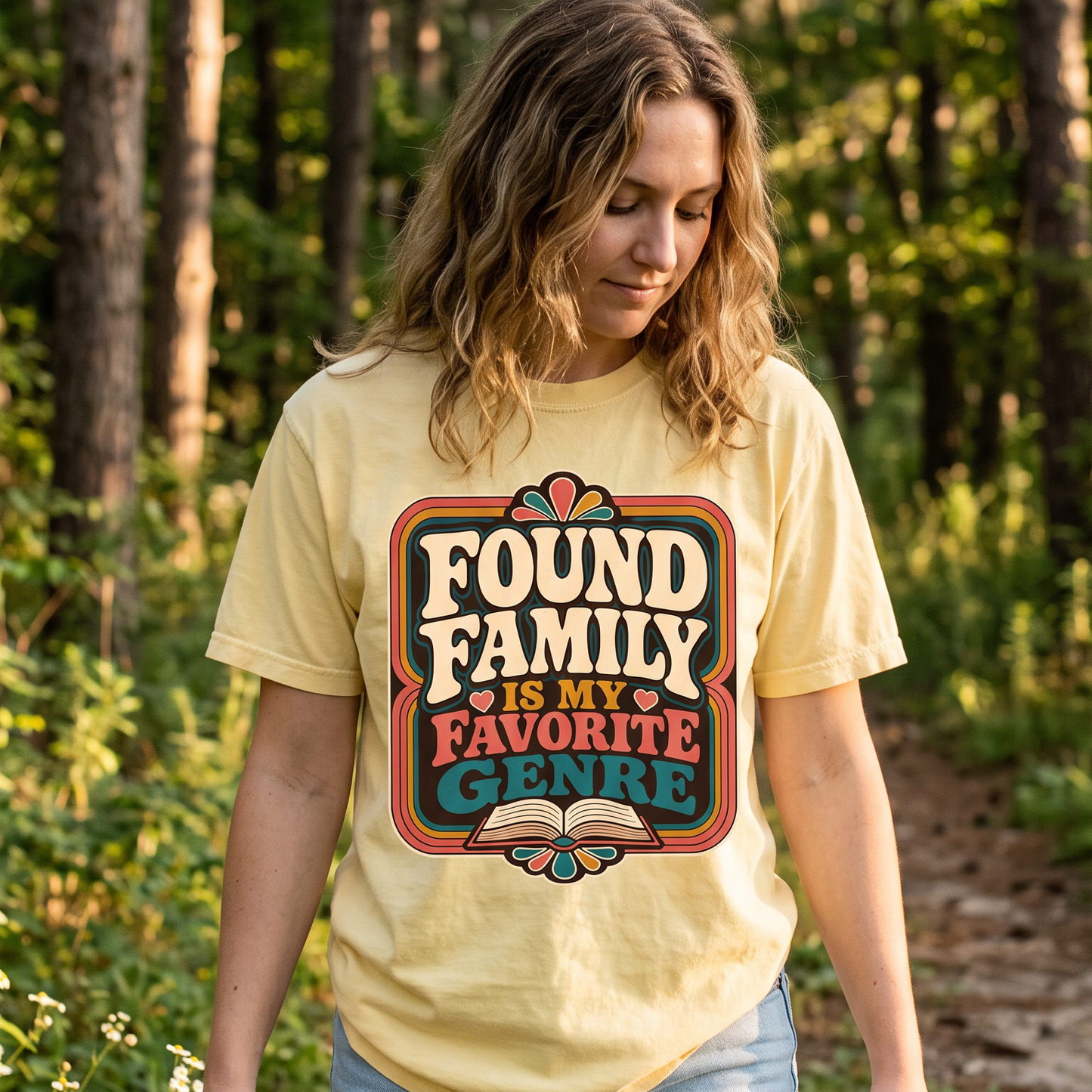 Woman wearing a Found Family Is My Favorite Genre book lover T-shirt outdoors in a woodland setting.