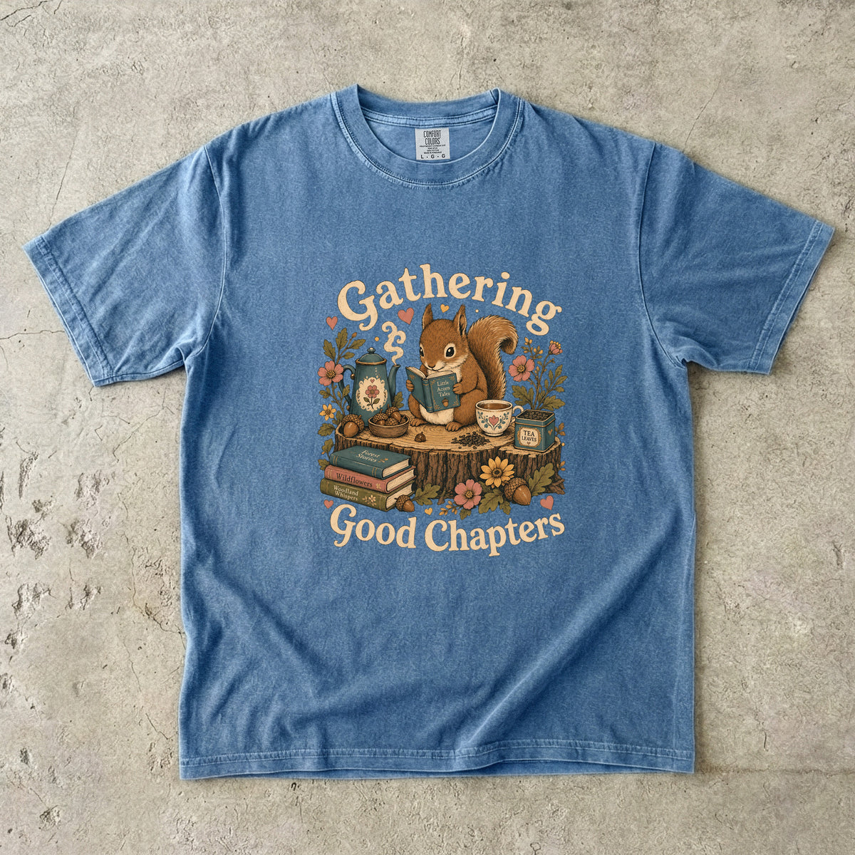 Gathering Good Chapters squirrel reading T-shirt in Blue Jean featuring a squirrel with a book, teapot, teacup, acorns and flowers