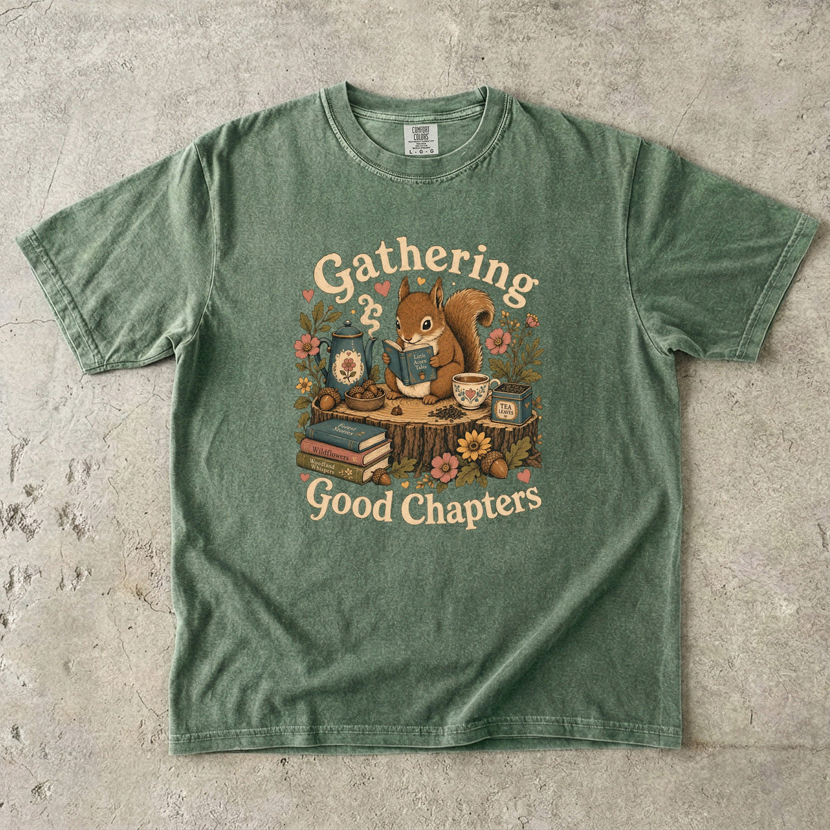 Gathering Good Chapters squirrel reading T-shirt in Moss featuring a squirrel with a book, teapot, teacup, acorns and flowers