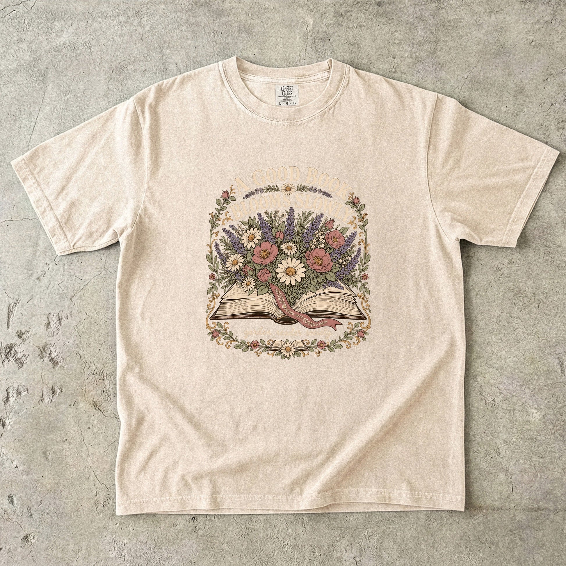 A Good Book Blooms Slowly botanical reading T-shirt with an open book and flowers on Ivory.