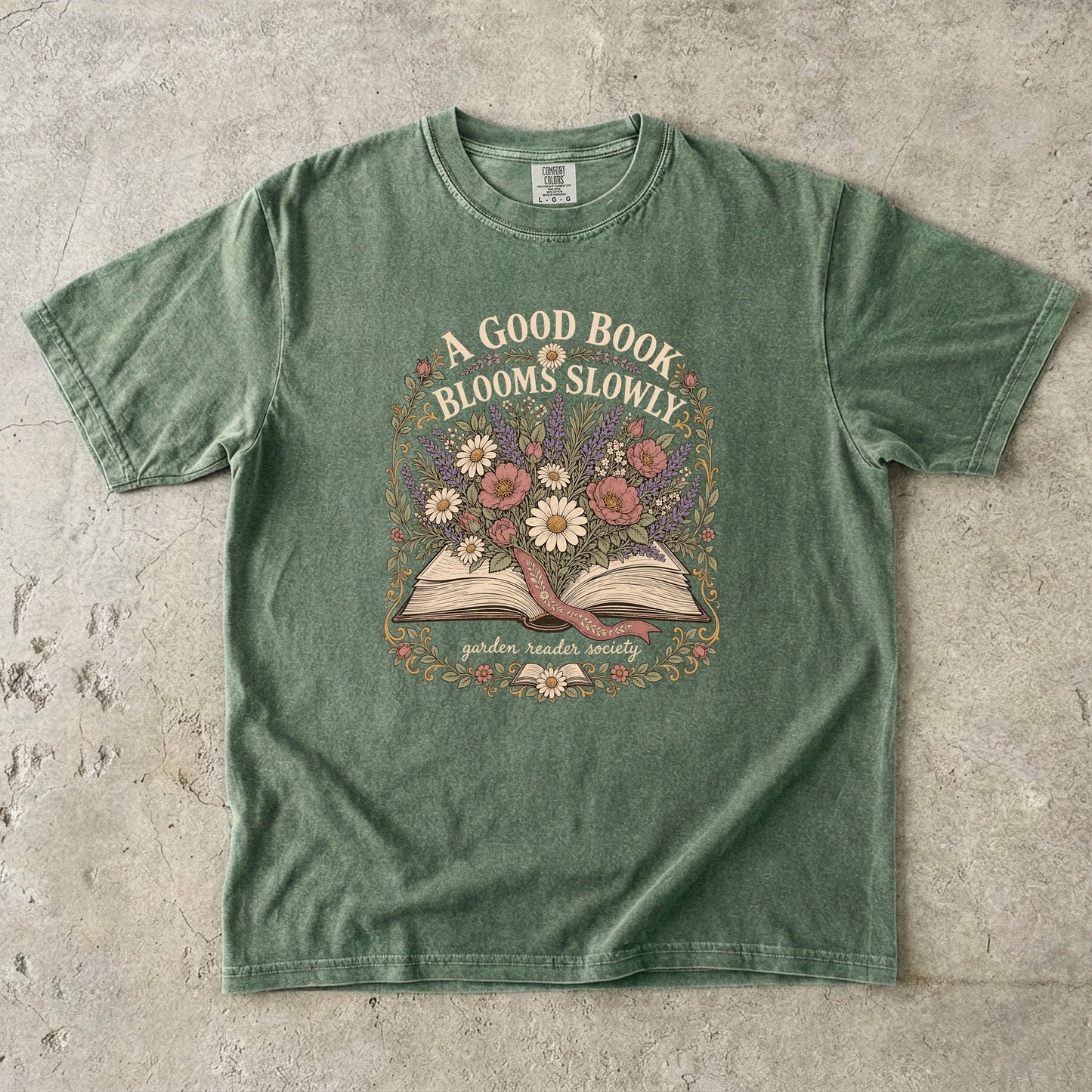 A Good Book Blooms Slowly botanical reading T-shirt with an open book and flowers on Moss.
