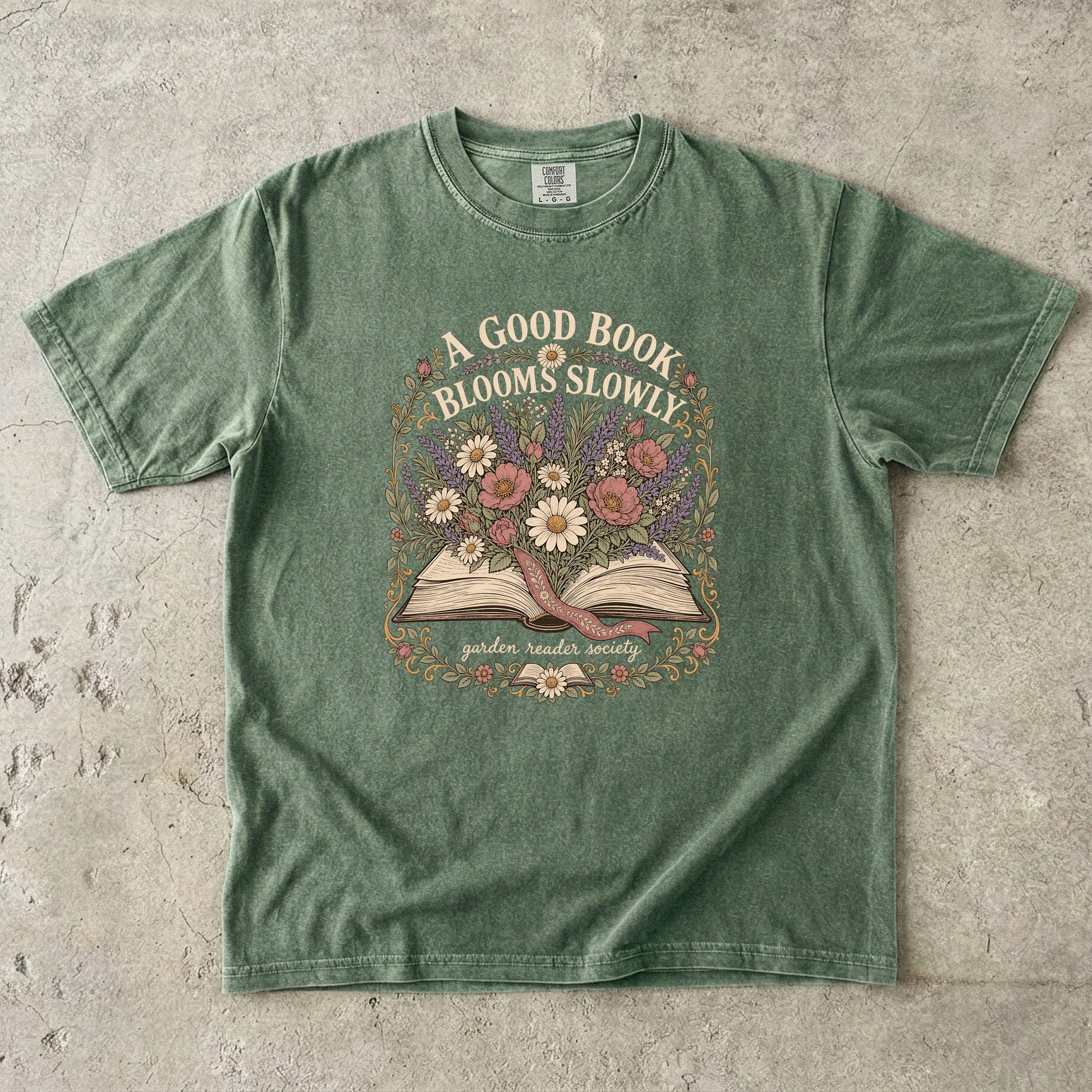 A Good Book Blooms Slowly botanical reading T-shirt with an open book and flowers on Moss.